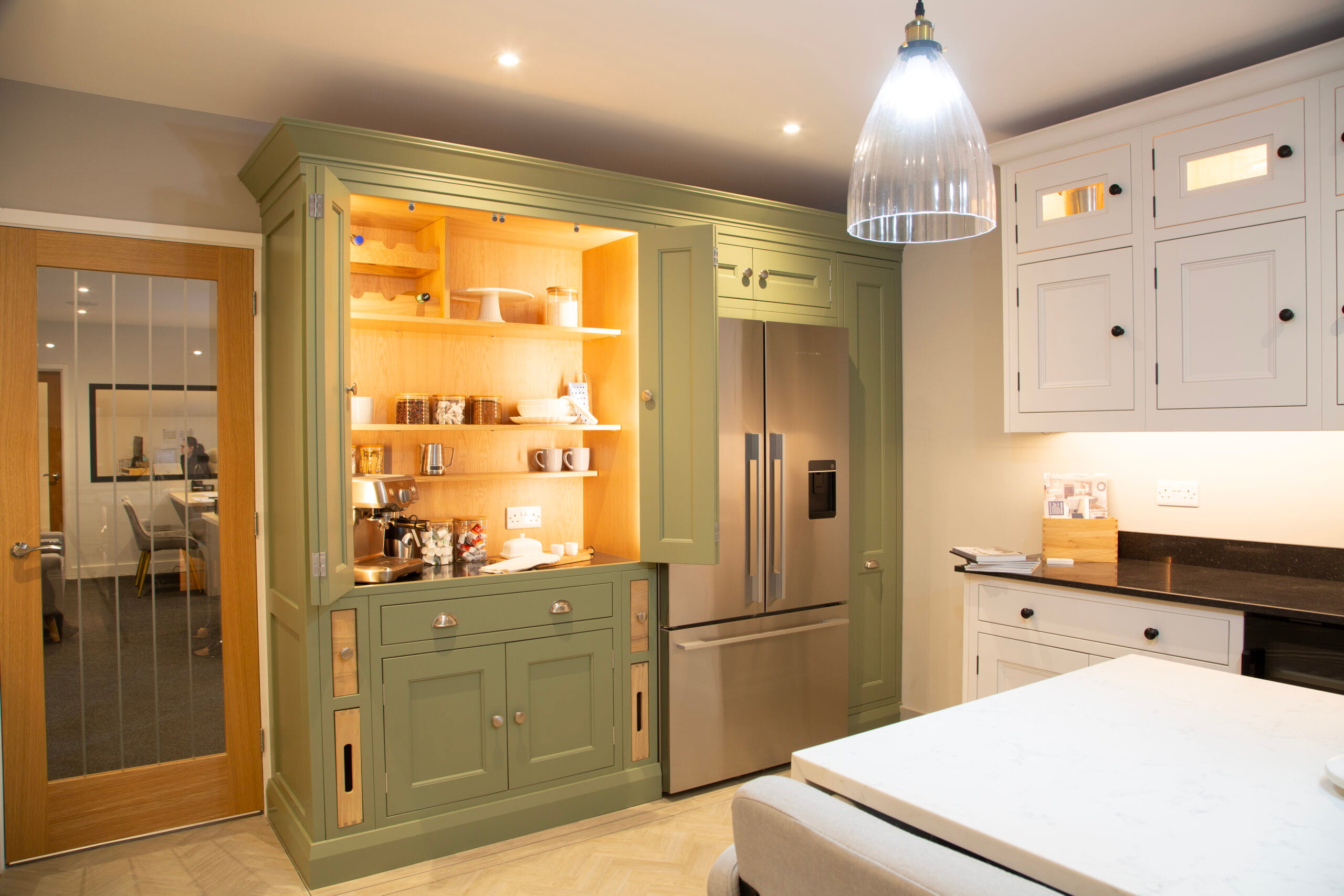 Made to measure kitchens by Regent St James Kitchens showing large kitchen showroom in Sage green finish and well lit pantry
