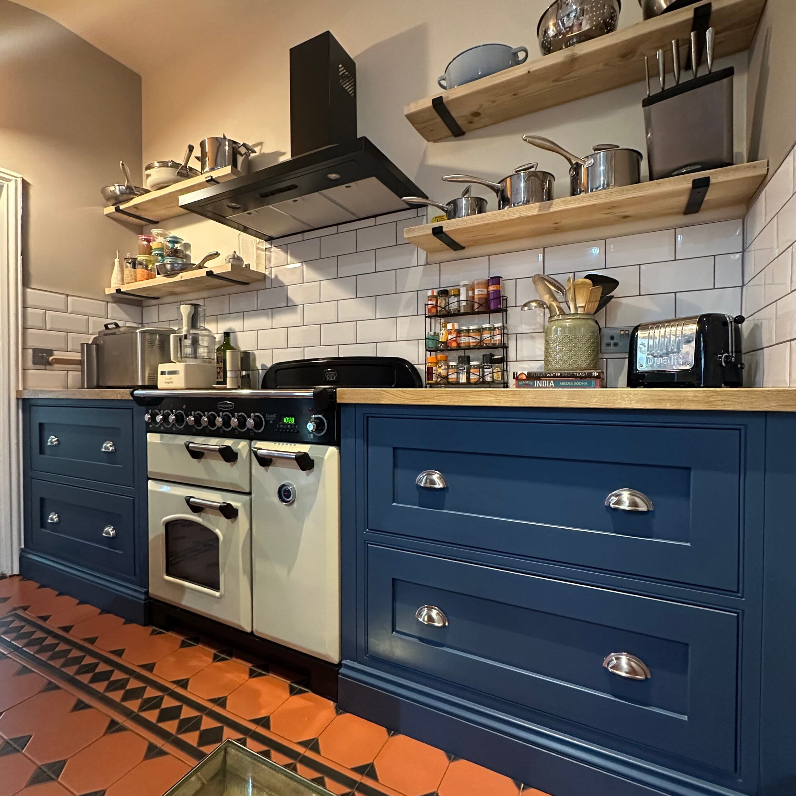 Bespoke kitchen in Gosfield with navy cabinets, range cooker, and oak shelving.