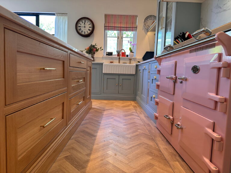 Bespoke Kitchen in Saffron Walden with oak cabinetry, pink range cooker, and herringbone flooring.