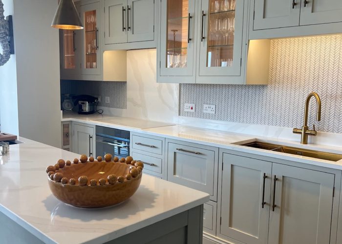 A kitchen with mint green kitchen cabinets, white Essex Granite worktops and Black handles on the cupboard doors.