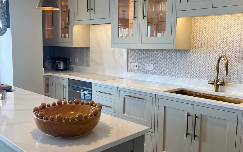 A kitchen with mint green kitchen cabinets, white Essex Granite worktops and Black handles on the cupboard doors.